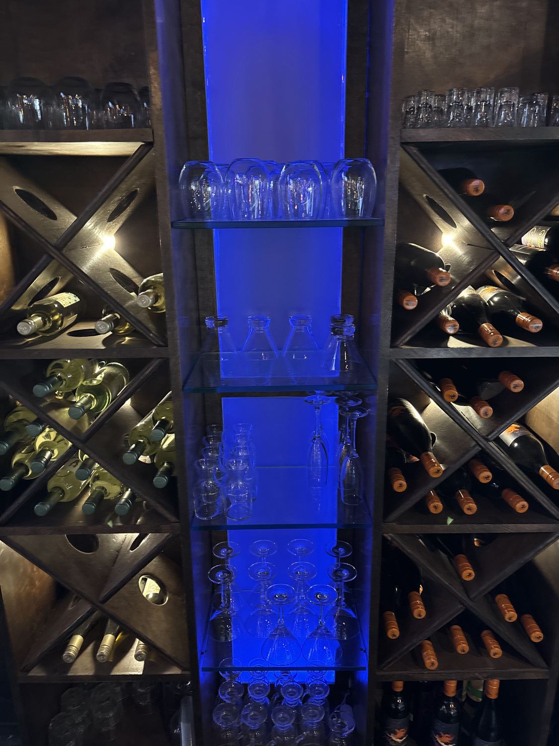 Wine racks lit blue behind the bar with glassware on the shelves