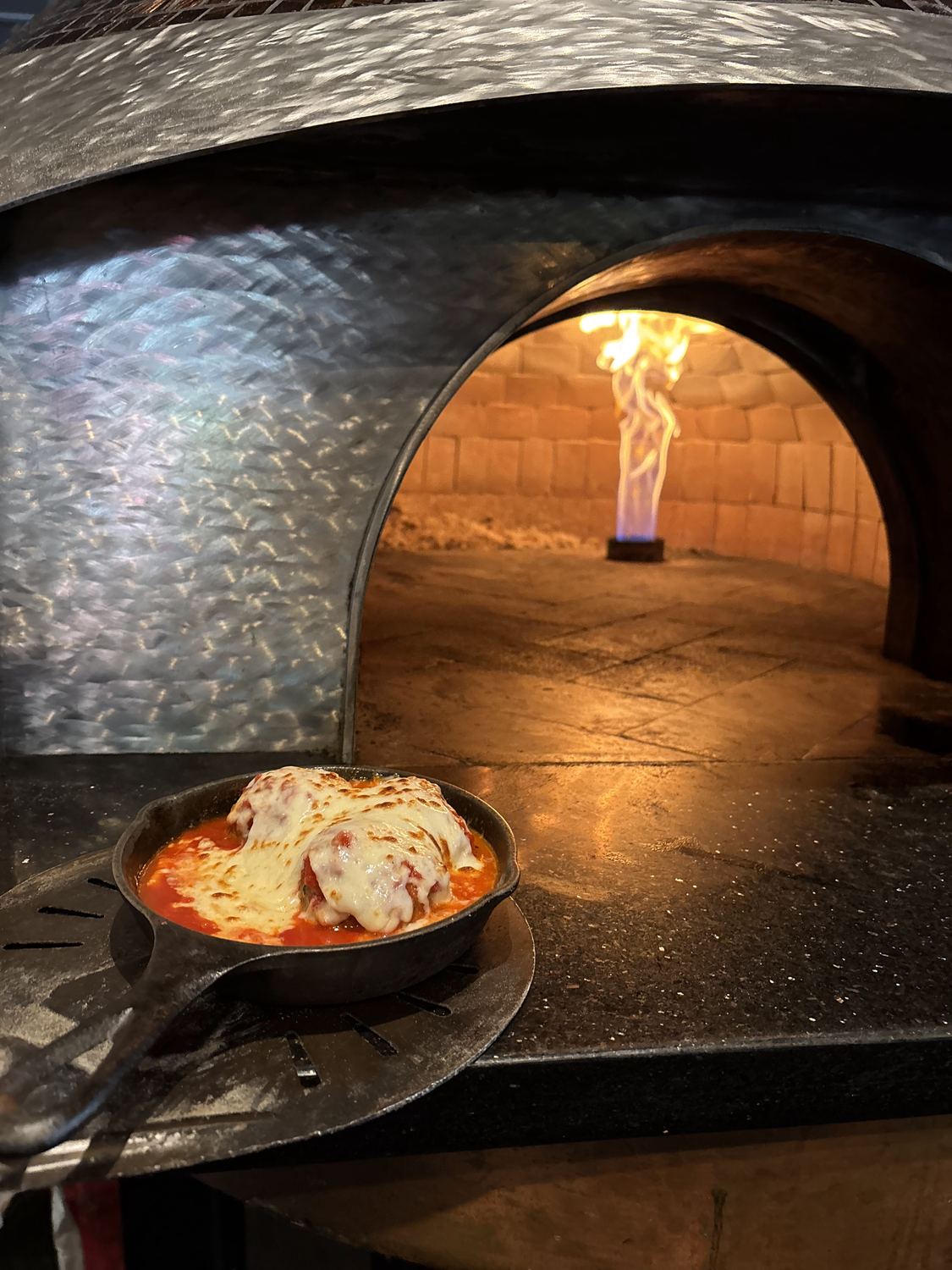 A cast-iron skillet of homemade meatballs going into the wood fire