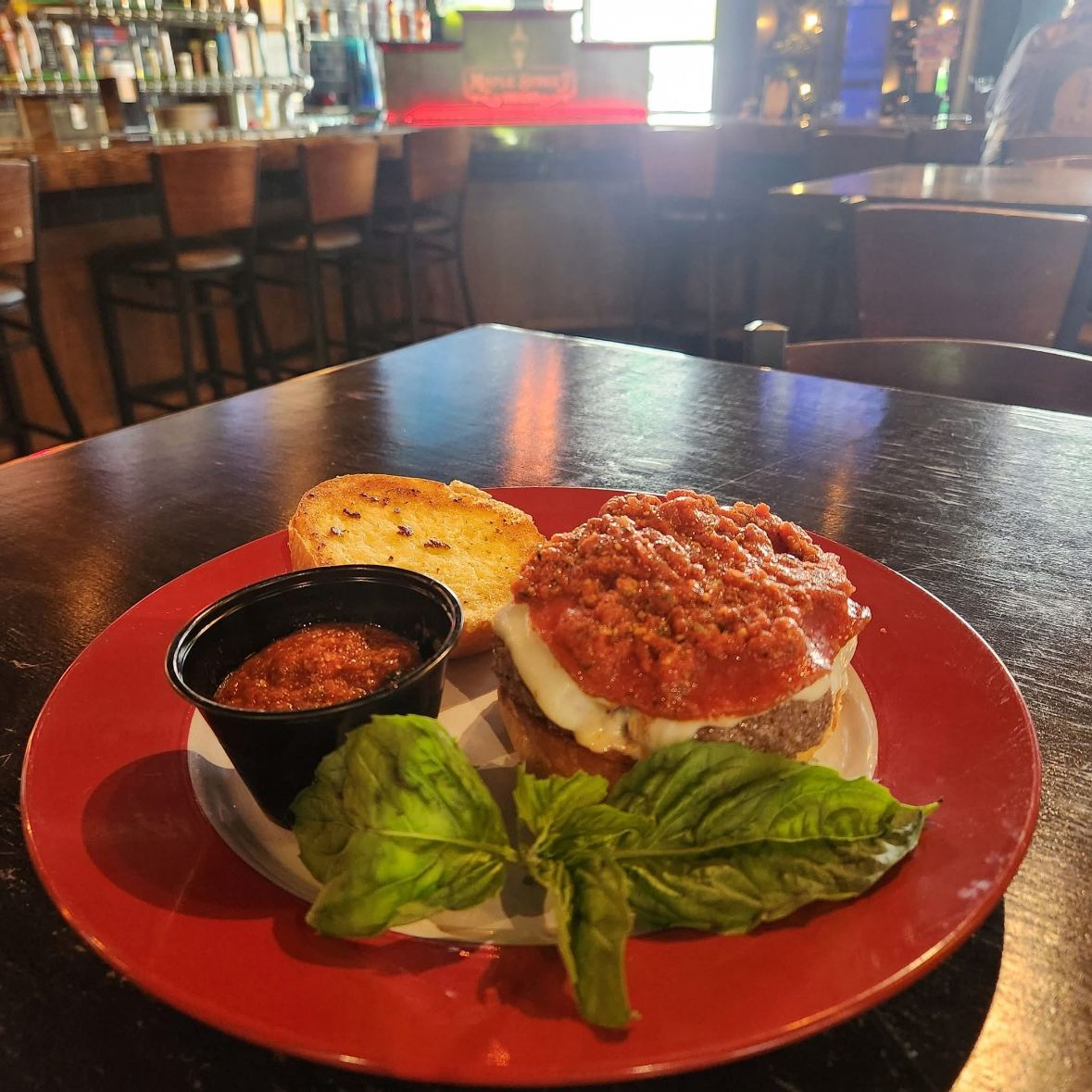 A parmesan burger with red sauce, melted cheese and garlic toast on a red plate
