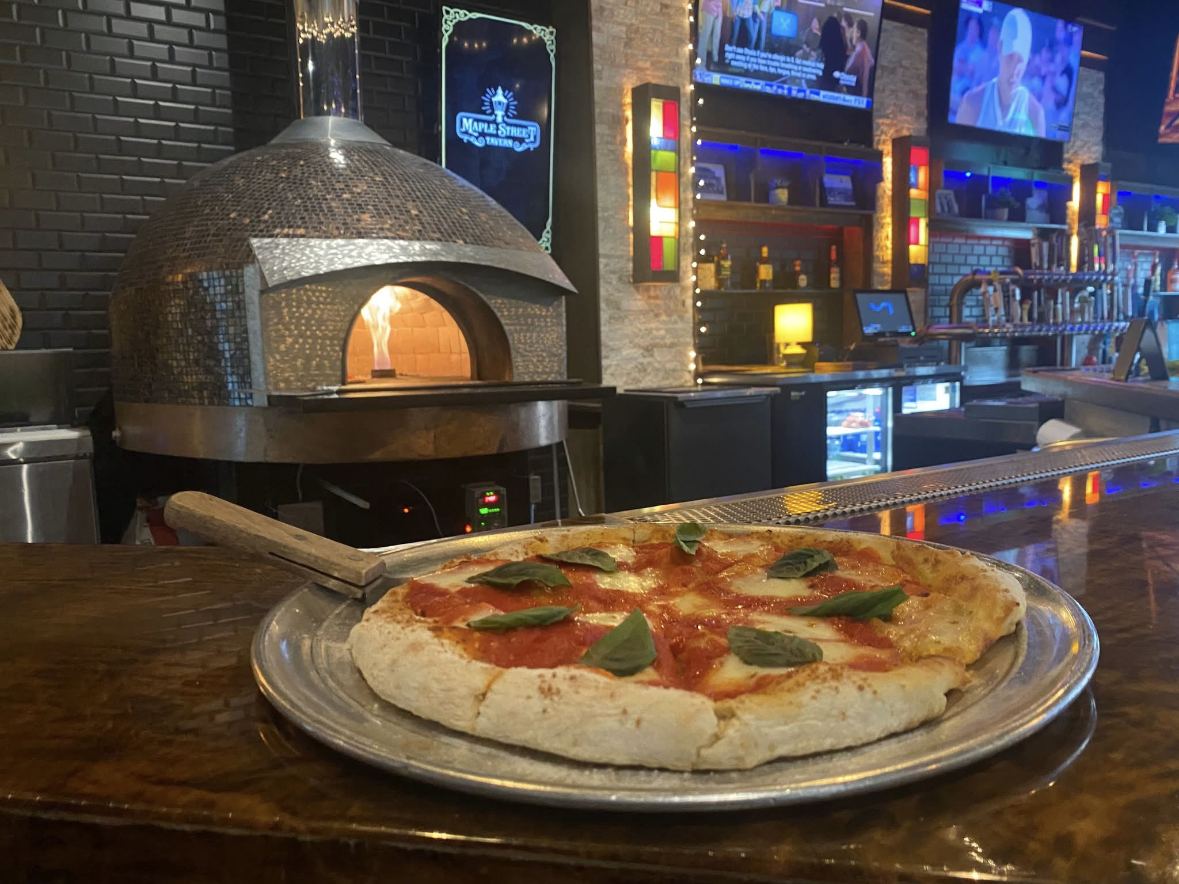 Margherita pizza on a peel in front of the lit brick oven