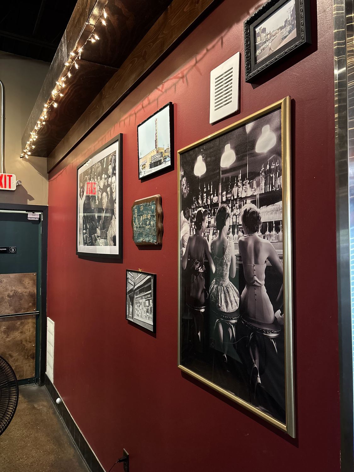 A red wall of framed vintage photographs under warm string lights